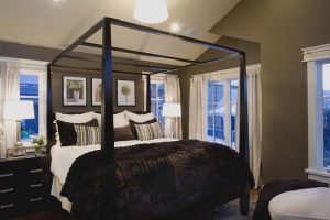 A bedroom with four poster bed and large windows.