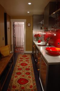 A kitchen with red counters and a rug.